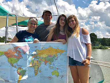 Molly Johnson, E’25, bioengineering and biochemistry, holding a world map on a sailboat with her parents and sister