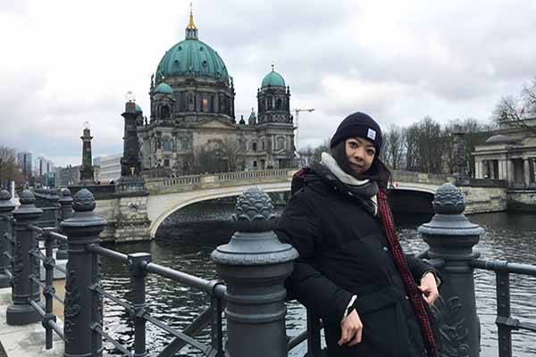 student in hat and coat in Berlin with building in the background